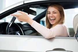 Happy young woman sitting in a car and holding new car keys while  looking at the camera.